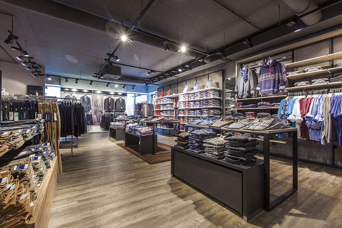 Innenansicht eines Modegeschäftes mit Regalen und Kleiderständern, gehängten und gelegten Textilien.