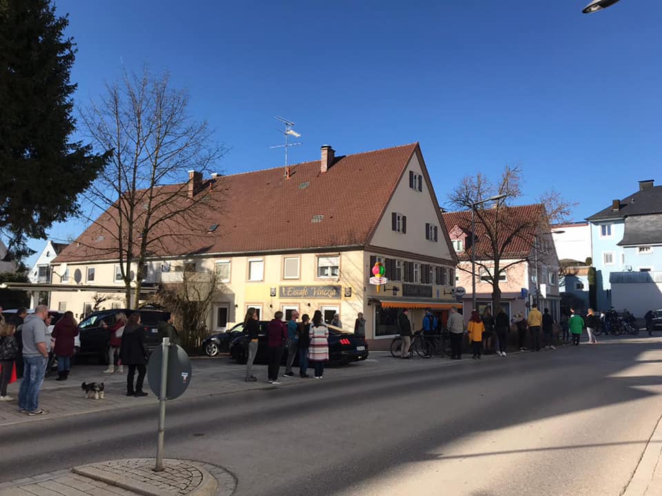 Ein beiges Gebäude mit Fensterläden und einer Markise im Untergeschoss. Viele Menschen gehen auf dem Gehweg davor.