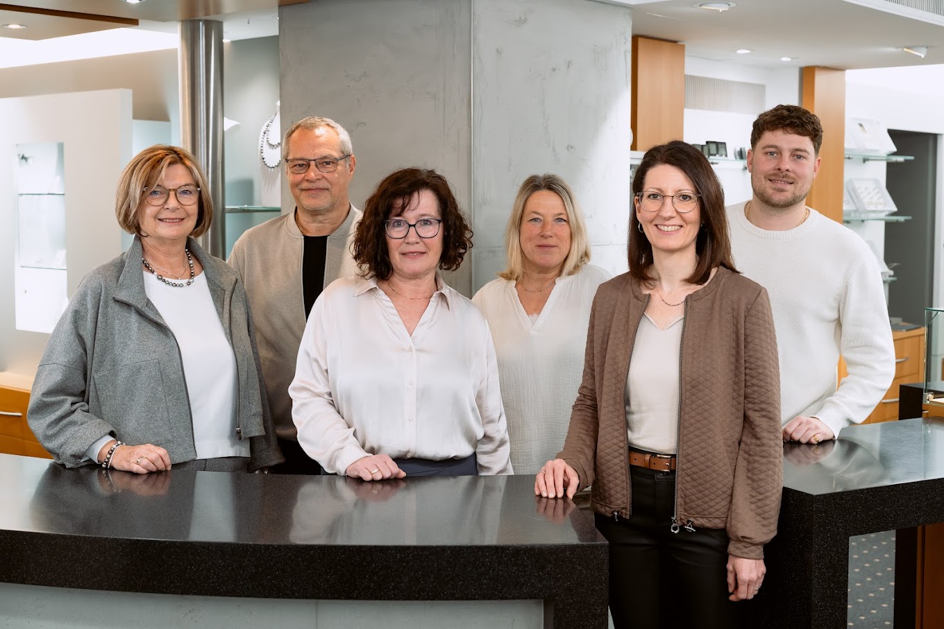 Gruppenfoto von 6 Personen, davon vier Frauen mittleren Alters, einem älteren Herren und einem jungen Mann in hinter einem modernen Verkaufstresen.