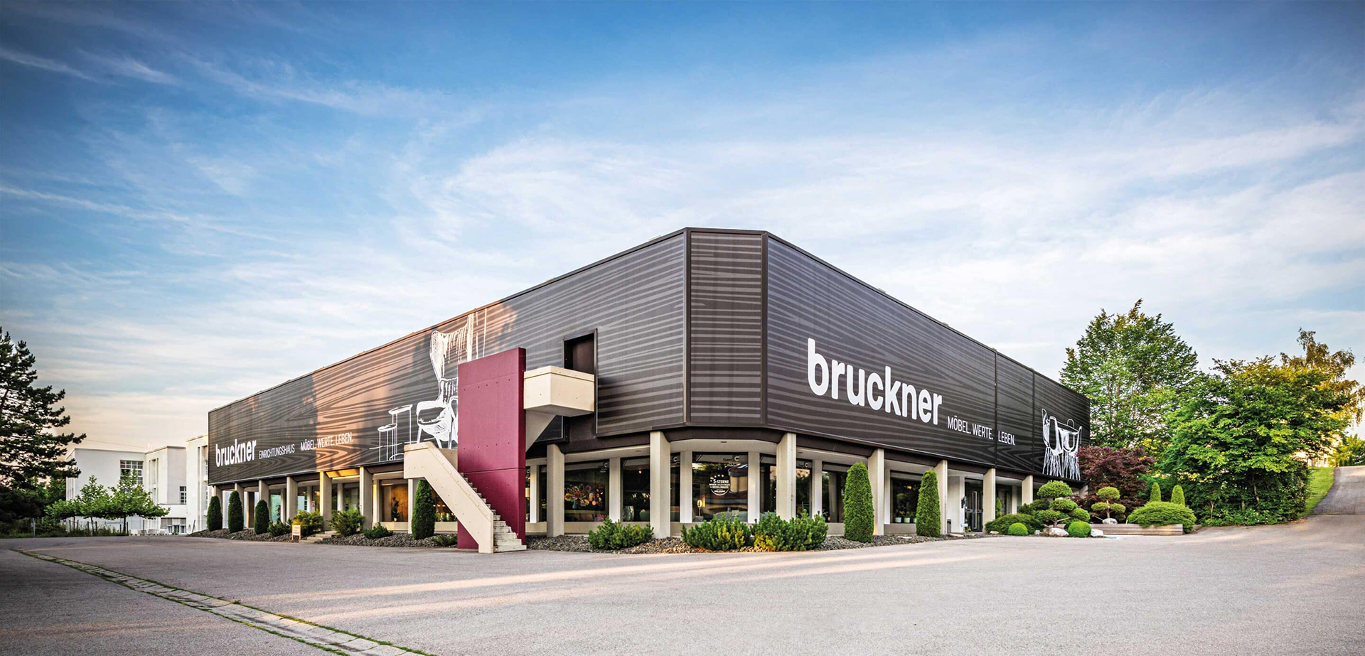 Außenansicht von einem Modernen Betongebäude mit Flachdach. Außenfassade mit übergroßer Holzmaserung, große Parkplatzfläche