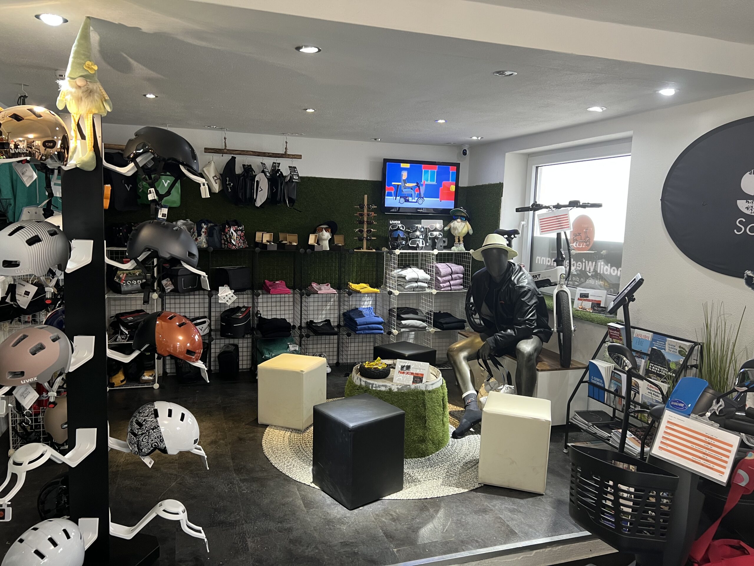 Ansicht eines Verkaufsbereichs mit Zubehör für Fahrräder, unter anderem Helmen. Ein kleiner Sitzbereich in der Ecke, die Kasse in der Hintergrund