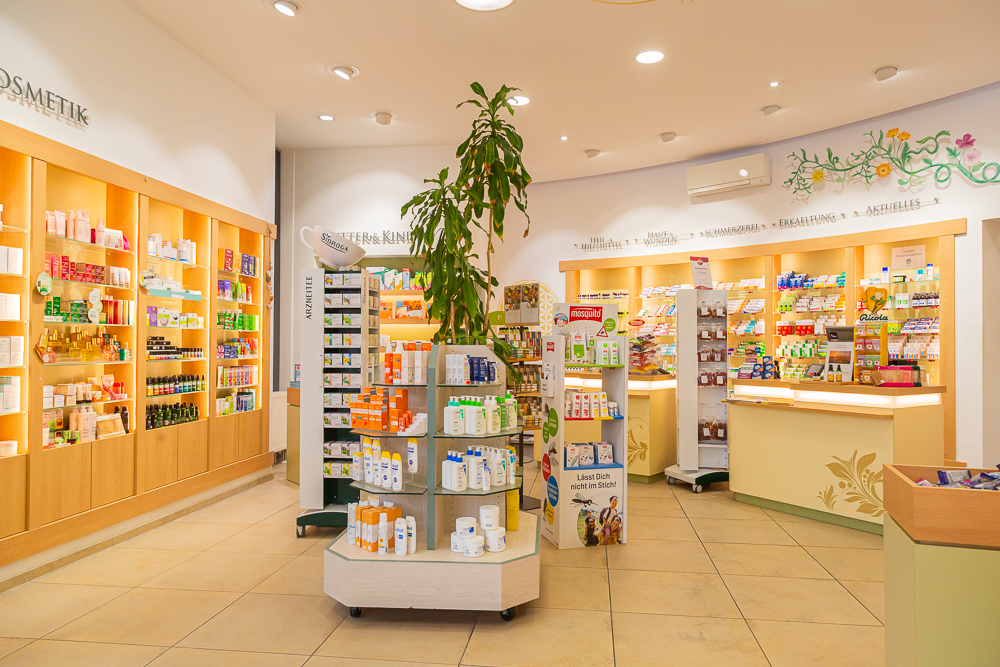 Verkaufsraum einer Apotheke mit Holzregalen an den Wänden und Theken in warmen Erdtönen.