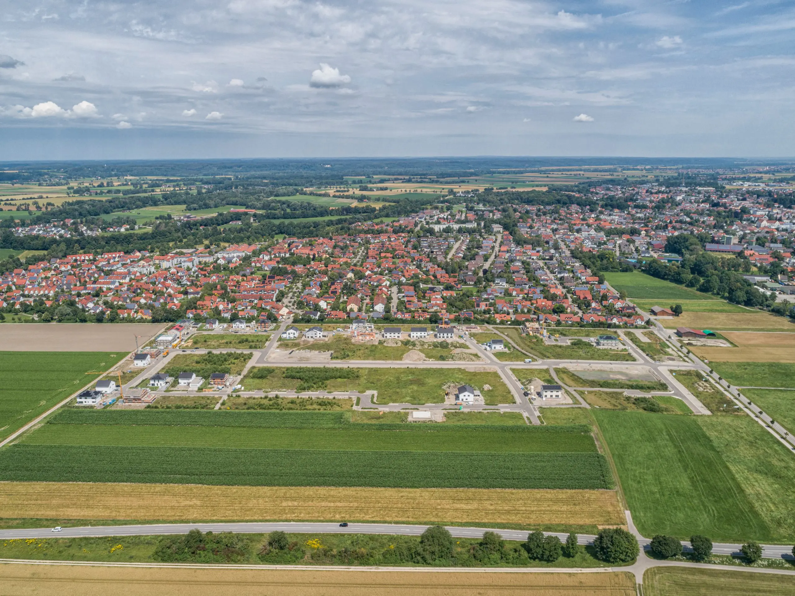 Luftaufnahme eines Stadtrandes mit Feldern und einem erst kürzlich erschlossenen, noch kaum bebautem Neubaugebiet mit Wohnhäusern.
