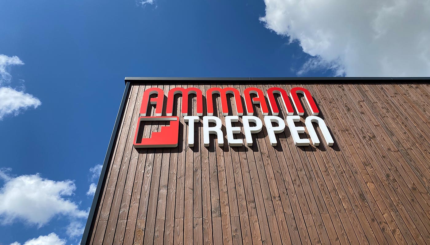 Eine Gebäudefront mit Holzfassade aus der Froschperspektive mit Firmenlogo vor blauem Himmel.