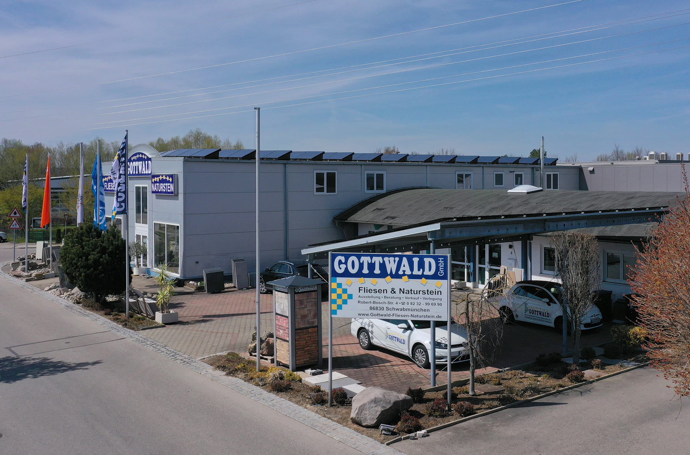 Ein Geschäftsgebäude im Industriegebiet mit überdachtem Parkplatz und verschiedenen Steinmustern und Pflastern außen. Leicht aus der Vogelperspektive aufgenommen.