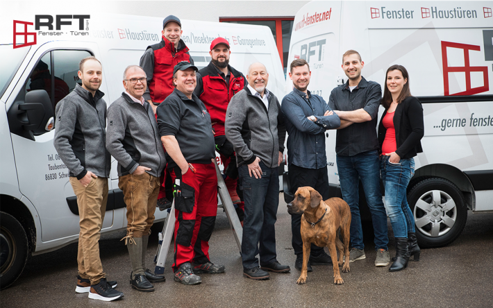 Ein Gruppenfoto von Menschen teilweise in roter Arbeitskleidung vor zwei weißen Transportern. Alle lächeln.